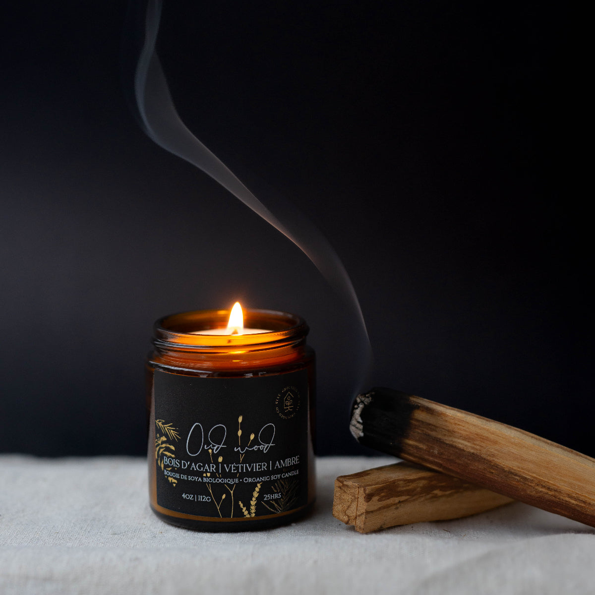 Diffuser une ambiance sophistiquée avec une bougie parfumée en cire de soya biologique aux notes de bois d'agar et ambre, offerte avec mèche de bois ou coton.