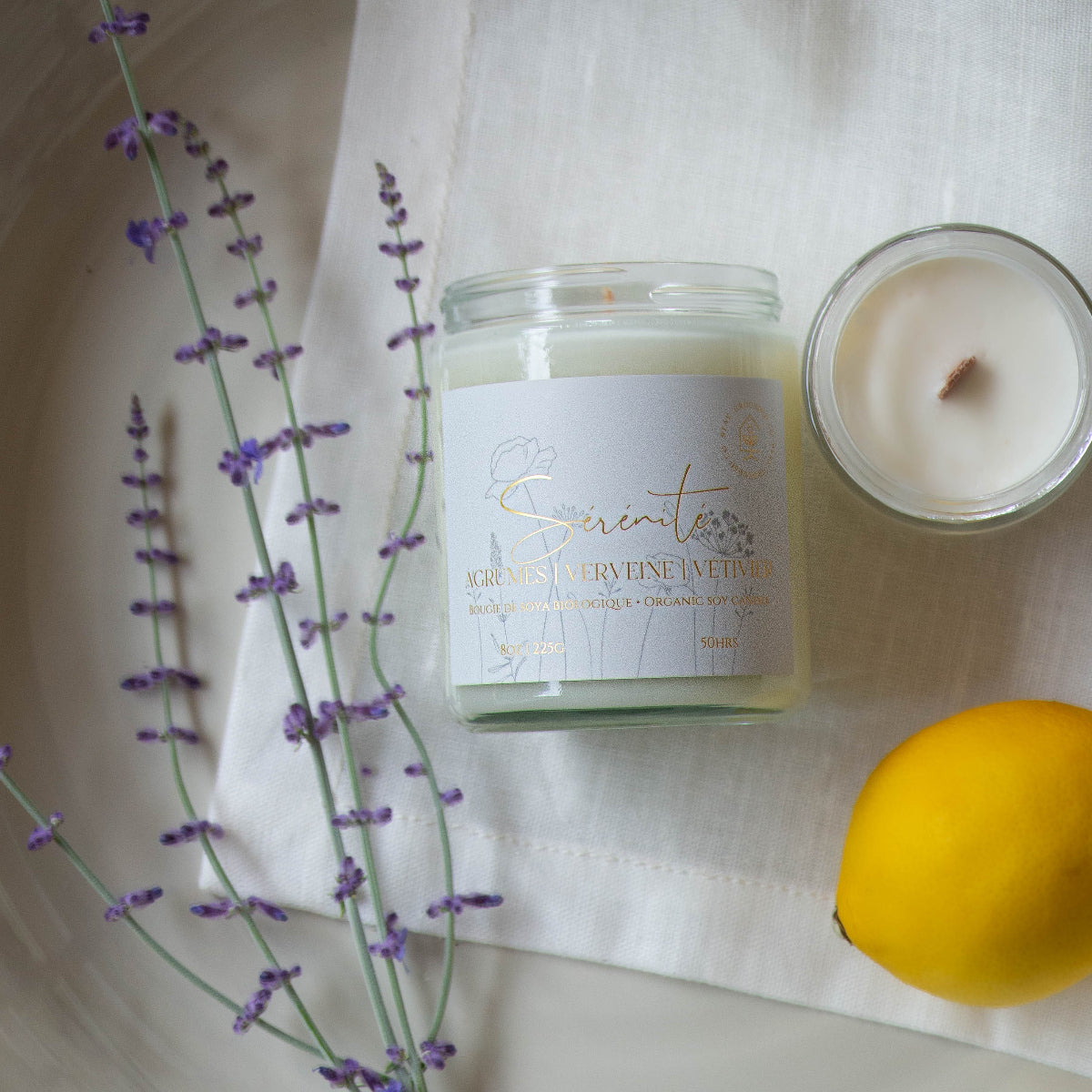 Diffuser une ambiance fraîche avec une bougie parfumée en cire de soya biologique aux notes de verveine et citron, offerte avec mèche de bois ou coton.